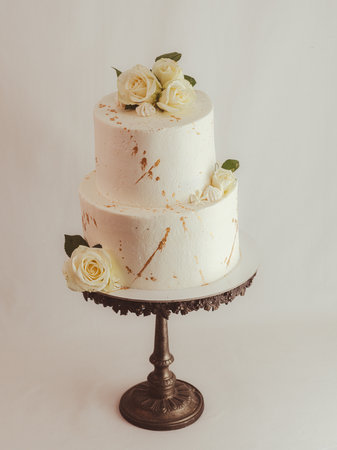 frosted tall cake with real roses and gold brush strokes of edible paint, isolated over white backgroundの写真素材