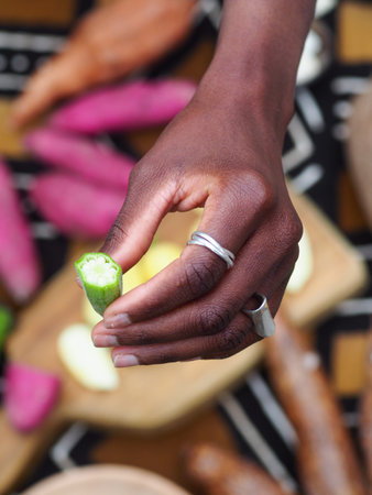 african woman chopping okra fruit veggies to cook traditional recipe with other local veggies and fruits.の写真素材
