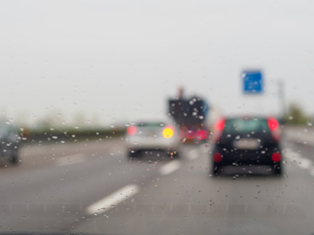 A blurry image of a busy street with cars and a truck. The rain is making the windshield of the cars and trucks wetの写真素材