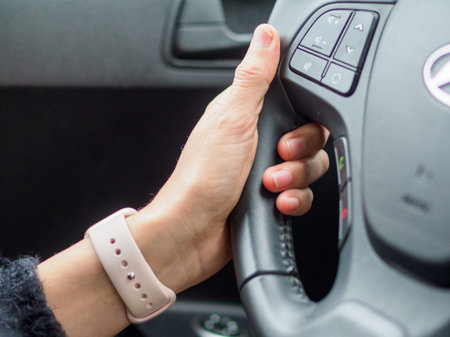 A woman is driving a car with a pink watch on her wrist. She is holding the steering wheel with both handsの写真素材