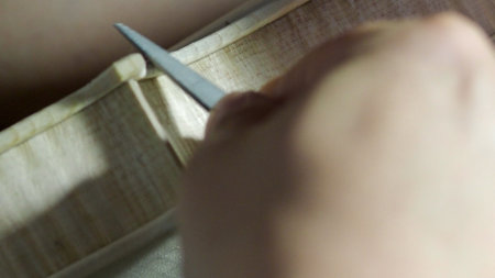Close up of a luthier's hands meticulously shaping the purfling of a violin using a chisel, showcasing the precision and craftsmanship involved in the creation of musical instrumentsの写真素材