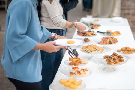 People enjoying a delicious buffet spread at an outdoor event with various appetizers and finger foods served on a long table creating a festive atmosphere for guestsの写真素材