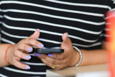 Cremona, Italy - July 21st 2025 Close up of hands holding a smartphone and typing using one hand showing polished fingernails and accessories like bracelets and ringsの写真素材
