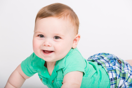 8 month year old baby lays on his stomach looking towards camerawith big smile. dressed in a cute green polo shirt and blue plaid shorts.の写真素材