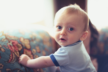 baby holding onto side of couch standing up looking at cameraの写真素材