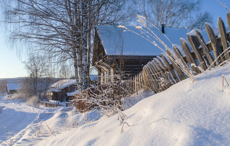 Rural landscape in winter - snow-covered village houses lit by the sun. Arkhangelsk region, Russia.の写真素材