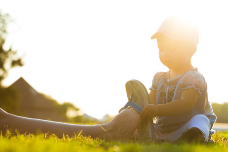 little baby in hat and dress is helping mother to put on shoesの写真素材