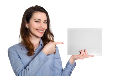 Positive smiling woman  in blue shirt pointing at blank piece of paper copy space isolated on white backgroundの写真素材