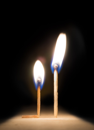 burning match kneeling before match on fire metaphor on black backgroundの写真素材