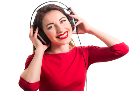 Girl in long-sleeve t-shirt wearing red lipstick touching big headphones listening to music smiling and looking at camera isolated on white backgroundの写真素材