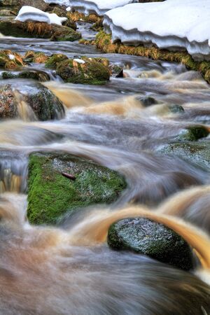 Waterfall with rocks and snow in forestの写真素材