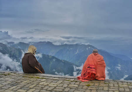 Two people sitting on the top of a mountain in the fog.の写真素材