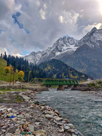 A panoramic shot of a bridge over a mountain river under a cloudy skyの写真素材