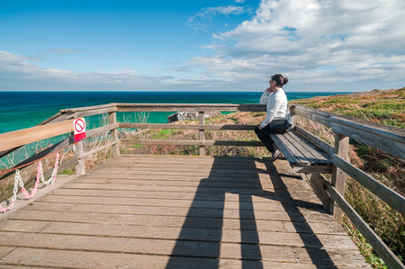 Woman contemplating ocean view from wooden viewpoint at as catedrais beachの写真素材
