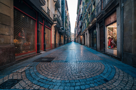 Narrow cobbled street winding through a traditional European city featuring historic buildings, closed shops, and an inviting pedestrian walkway, hinting at urban explorationのeditorial素材