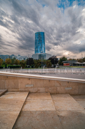 Urban landscape showing the modern blue glass skyscraper of Sky Tower rising against a cloudy sky, with beige stone steps and water fountains in the foregroundのeditorial素材
