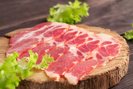Appetizing red ham, sliced on a natural wooden plateau on the background of rough textured aged boards. A shot of cold cuts in blur with selective focus.の写真素材