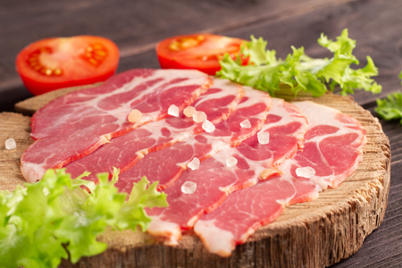Gorgeous delicious slicing of jamon on a natural wooden plateau with greens, tomatoes and Himalayan salt. Luxury elite premium snack.の写真素材