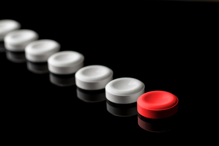 Behind the red pill are lined up white pills. One red and many white pills on a black background. With blur in perspective. Concept on leadership and features. From left to right. Top down.の写真素材