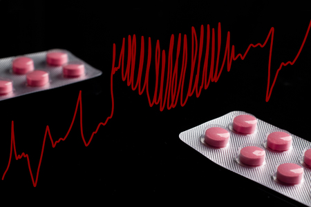 Two blisters with red pills on a black acrylic background with a red heart-shaped cardiogram. Concept on drugs with heart cardiogram. Dark background with shiny blisters and red pills.の写真素材