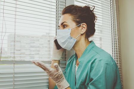 Doctor italian woman in medical mask, gloves and doctors suit closed her eyes and talking on a cell phoneの写真素材