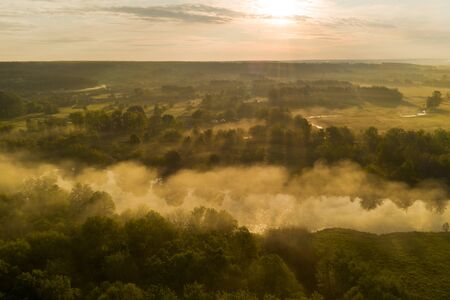 Gorgeous warm spring landscape: Fog over a small river among forest green treesの写真素材