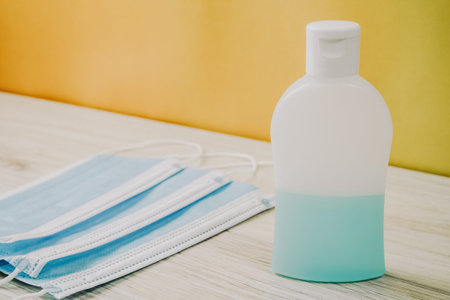 Blue Alcohol sanitizer hand spray in a white plastic vial and several medical surgical masks to...