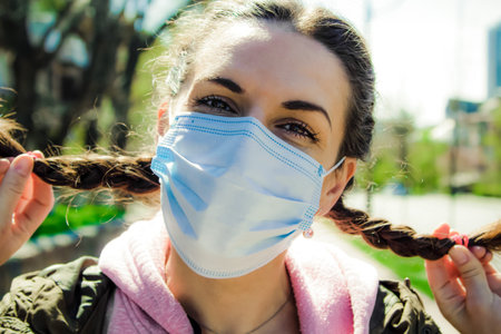 The face of a smiling young woman in a mask with pigtails of hair in the street.