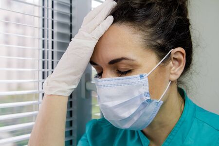 Tired Doctor italian woman in medical mask, gloves and doctors suit closed her eyes and propped her head against fatigue.の写真素材