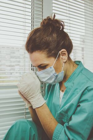 Tired Doctor woman in medical mask, gloves and doctors suit closed her eyes and prayingの写真素材