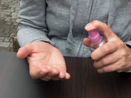 A woman handles her hands with a spray disinfecter before eating at a summer cafe.の写真素材