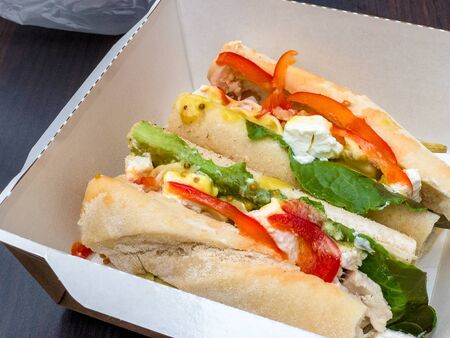 Street food: sandwich with chicken, salad, feta cheese, Bulgarian pepper in mustard-honey sauce in a cardboard disposable box.の写真素材