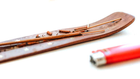 Burnt aromatic sticks on a brown wooden stand next to a lighterの写真素材