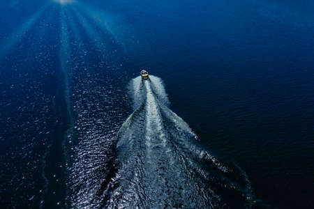 The boat sails away on the waves of the blue sea, cutting through the waves.の写真素材