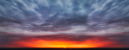 Symmetrical epic grotesque sky with bright scarlet sun at sunset among dark cloudsの写真素材