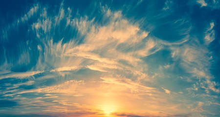 The sun at the edge of the horizon paints white clouds on the blue sky in golden color: Sunny sunsetの写真素材