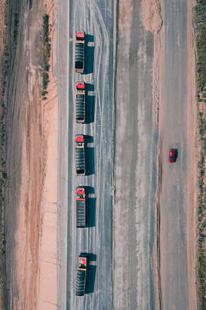 Convoy of trucks driving on asphalt road with one red car on another side of road, top viewの写真素材