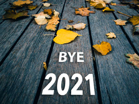Bye 2021 inscription on a wooden autumn background with yellow leaves.の写真素材