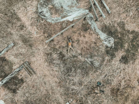 Soldier lies on the dry grass and prepares to fire a weapon - aerial overhead top view drone shotの写真素材