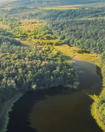 House on plot on the shore of a large lake among green forests with trees - aerial drone shotの写真素材