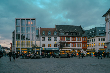 People walk in city square by buildings under skyのeditorial素材