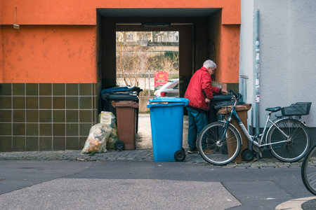 An elderly woman sorts garbage into various containers near the house.のeditorial素材