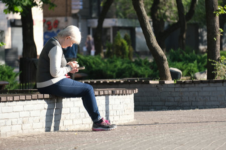 Elderly woman sits on a bench looking at her phoneのeditorial素材
