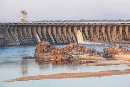 Experience the Stunning and Magnificent View of a Dam, with Flowing Water and Rocky Shorelineの写真素材