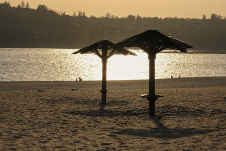 Experience a tranquil sunset at the beach, with soothing palm shade structures enhancing the sceneの写真素材