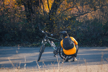 A mountain biker in a bright orange shirt crouches beside his bike, adjusting gear amidst vibrant fall foliage.の写真素材