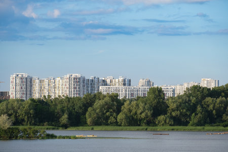 This breathtaking and stunning scene beautifully portrays modern apartments located by a tranquil water body, which is encircled by vibrant and lush trees set beneath a serene blue skyの写真素材