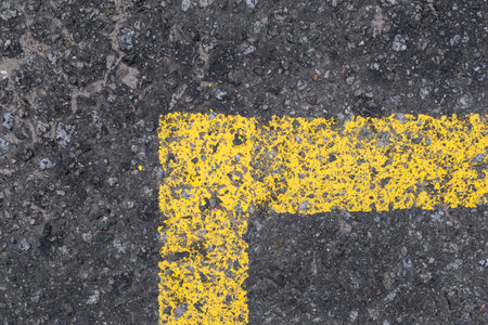 This closeup shows a weathered yellow parking line on textured asphalt, highlighting the contrast between the vibrant paint and the rough pavement, creating a visually appealing detailの写真素材
