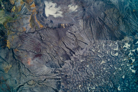 Aerial view of textured volcanic terrain with erosion patterns and mineral deposits forming abstract natural shapes. The image captures the beauty of geological formations from aboveの写真素材