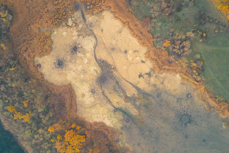aerial view abandoned sand pit with shallow ponds and scattered yellow shrubs, exposed pale sand...